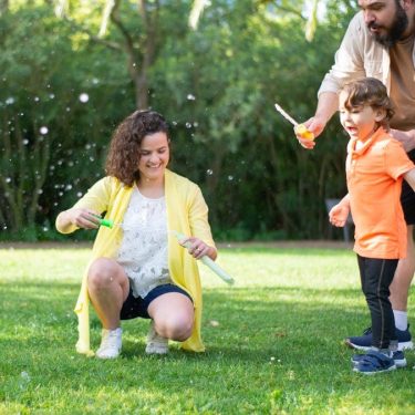 A family enjoys a playful day with bubbles in a sunny park setting.